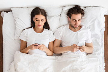 Couple Using Mobile Phones Lying In Bed At Home, Top-View