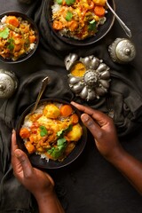 Hands cupping a bowl of chicken curry with potatoes against a black backdrop