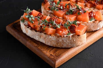 bruschetta with salmon, cottage cheese, dried tomatoes and micro greens, on a black background
