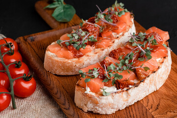 bruschetta with salmon, cottage cheese, dried tomatoes and micro greens, on a black background