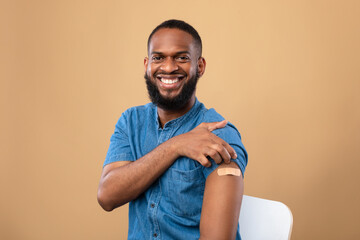Happy vaccinated black man showing shoulder with band aid after coronavirus vaccine shot, posing...
