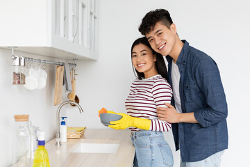 Pretty asian lady washing dishes, wearing gloves