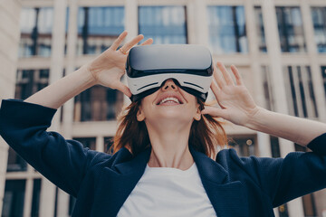 Immersed woman looking up in virtual reality while wearing portable VR, standing on city street © VK Studio