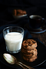 Stack of cookies and glass of milk on dark background. Rustic food photography.