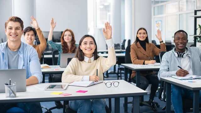 Portrait of diverse students raising hands at classroom
