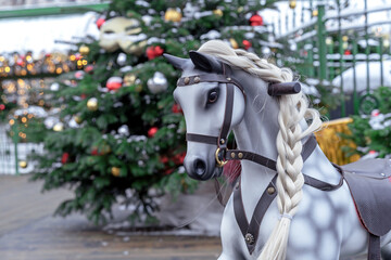 Children's rocking horse with a white braided mane against the background of a Christmas tree.