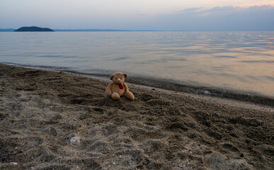 Teddy bear sits on the sand and watches the sunset. The sunset in Greece. 