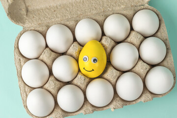 Top view of a box with white eggs and one egg yolk with eyes.