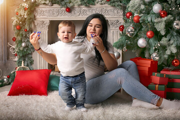 a brunette girl in a white T-shirt hugs her little son sitting by the Christmas tree fireplace