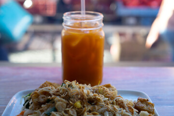 Close up of thai iced tea in a glass jar with a straw and pad thai