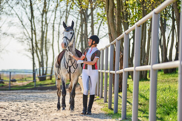 Beautiful horse rider girl stands near a horse on a farm 