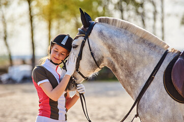 Beautiful horse rider girl stands near a horse on a farm 