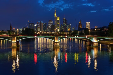 Fototapeta na wymiar Frankfurt am Main, Germany. View from a bridge across the Main to skyscrapers of financial district in twilight. Tower of Frankfurt Cathedral is visible to the right of the skyscrapers.