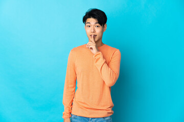 Young Chinese man isolated on blue background showing a sign of silence gesture putting finger in...