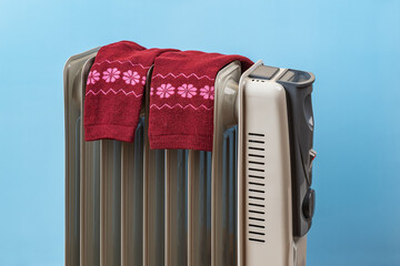Red warm socks on a hot oil filled electric heater against blue background. Dangerous using of 9...