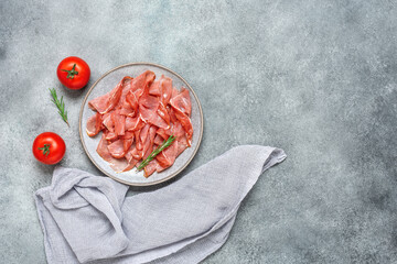 Slices of prosciutto crudo parma or jamon serrano on gray grunge background. Top view, flat lay.