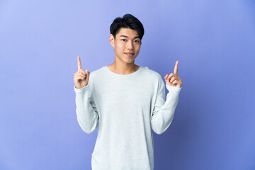 Young Chinese man isolated on purple background pointing up a great idea