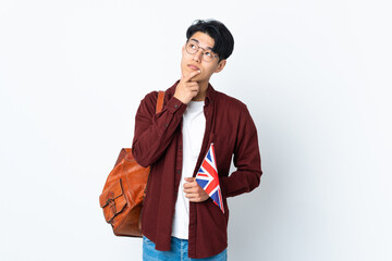 Chinese man holding an UK flag isolated on purple background having doubts