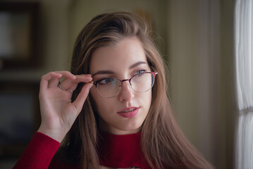 Young girl in the glasses and red dress is looking in the window.