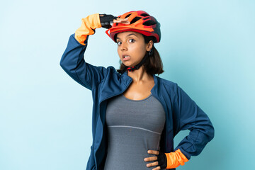 Young cyclist woman isolated on blue background doing surprise gesture while looking to the side - obrazy, fototapety, plakaty
