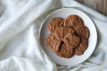 Plate of healthy, gluten free and high protein cookies, made with bananas, eggs, chia seeds and almonds. White tablecloth and wooden background. Flat lay.