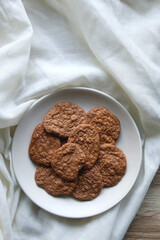 Plate of healthy, gluten free and high protein cookies, made with bananas, eggs, chia seeds and almonds. White tablecloth and wooden background. Flat lay.