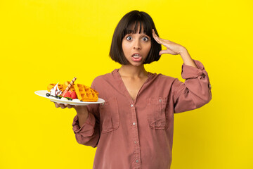 Pregnant woman holding waffles isolated on yellow background with surprise expression