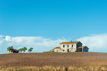 Abandoned house on the hill. Brick building covered with red tiles, broken windows and doors. Around the plowed field.and some green trees