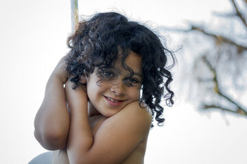 Ni&ntilde;a de cabello negro rizado feliz agarrada a una barra en verano sonriendo y mirando a la c&aacute;mara.