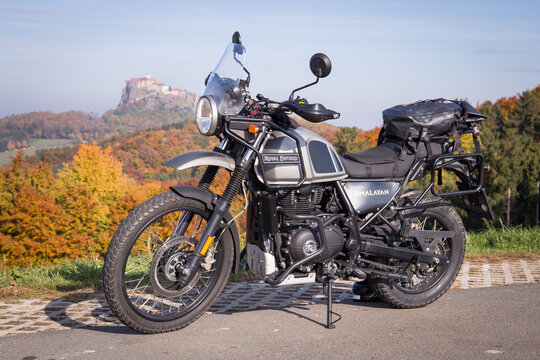 Classic Royal Enfield motorcycle parked in front of a colorful autumn forest with the riegersburg castle in the background