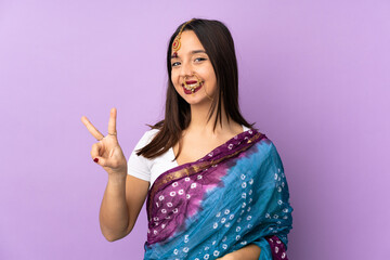 Young Indian woman isolated on purple background smiling and showing victory sign