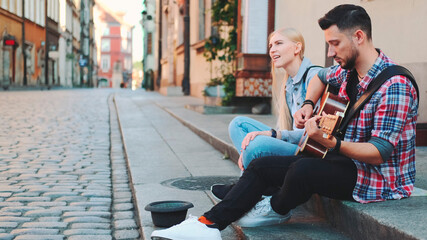Young man and woman of street singers sitting on sidewalk, playing guitar and singing. Lifestyle concept.