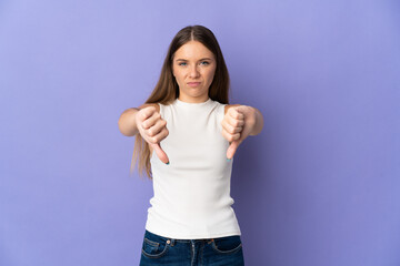 Young Lithuanian woman isolated on purple background showing thumb down with two hands