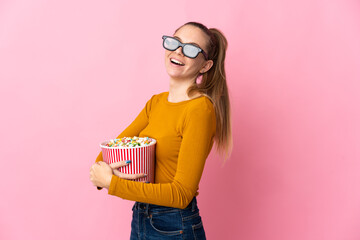 Young Lithuanian woman isolated on pink background with 3d glasses and holding a big bucket of popcorns