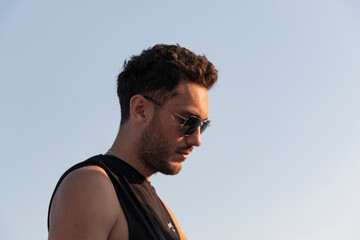 Obraz premium Fit, handsome boy with sun glasses. He is on summer vacation. Thoughtful face. He is looking down. Sunlight. Cover boy. Copy and text space. 