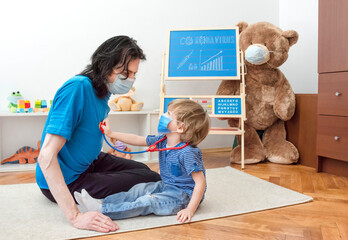 Cute child boy in home quarantine using stethoscope toy, playing doctor with dad wearing medical...