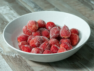 frozen strawberries in a white bowl on a wooden table, a lot of details, macro photo
