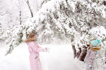 Mom and daughter in warm winter overalls for a walk in the winter forest: active games, playing snowballs and other activities