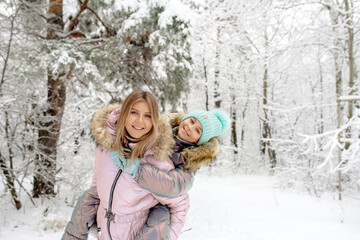 Fototapeta premium Mom and daughter in warm winter overalls for a walk in the winter forest: active games, playing snowballs and other activities