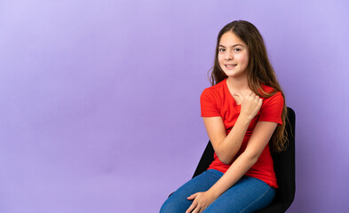 Little caucasian girl sitting on a chair isolated on purple background proud and self-satisfied