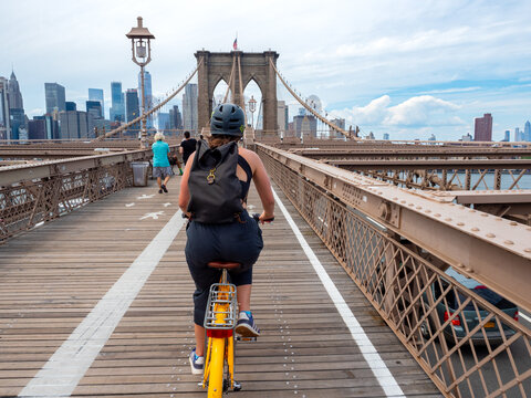 Woman Riding A Yellow Bike Across The Brooklyn Bridge With A View From Behind