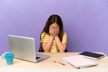 Little student girl in a workplace with a laptop isolated on purple background with tired and sick expression