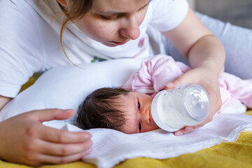 Obraz na płótnie Canvas Close up on caucasian baby infant two weeks old in hands of her mother drinking from bottle feeding artificial milk formula food - health and nutrition parenting and newborn healthy food concept