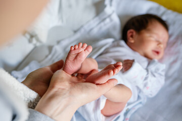 Close up on hands of unknown woman holding feet of her newborn baby son or daughter infant child in day - motherhood and maternity love concept copy space