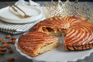 A traditional French galette des rois on a plate with crown, with a cut piece and its fève in a middle. Made puff pastry and creamy almond filling roll in circle shape. It's usually served on Epiphany