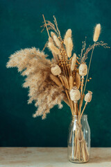 Bouquet of beige dried flowers in a glass vase on green blue background. Home decoration concept.