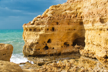 Towering limestone cliffs with lots of caves rise up from a stormy sea. Algar Seco, Carvoeiro, Algarve, Portugal