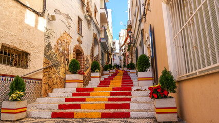 Fototapeta na wymiar Calle con escalones con los peldaños pintados con la bandera de España en la localidad alicantina de Calpe en España.