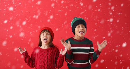Cute little children in winter sweaters catching falling snow with their tongues on color background