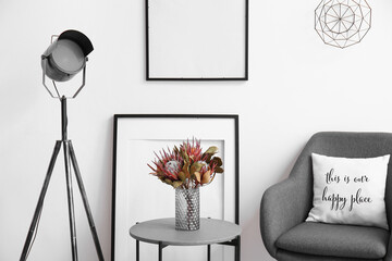 Closeup of stylish interior with lamp, blank picture frames, coffee table and modern armchair